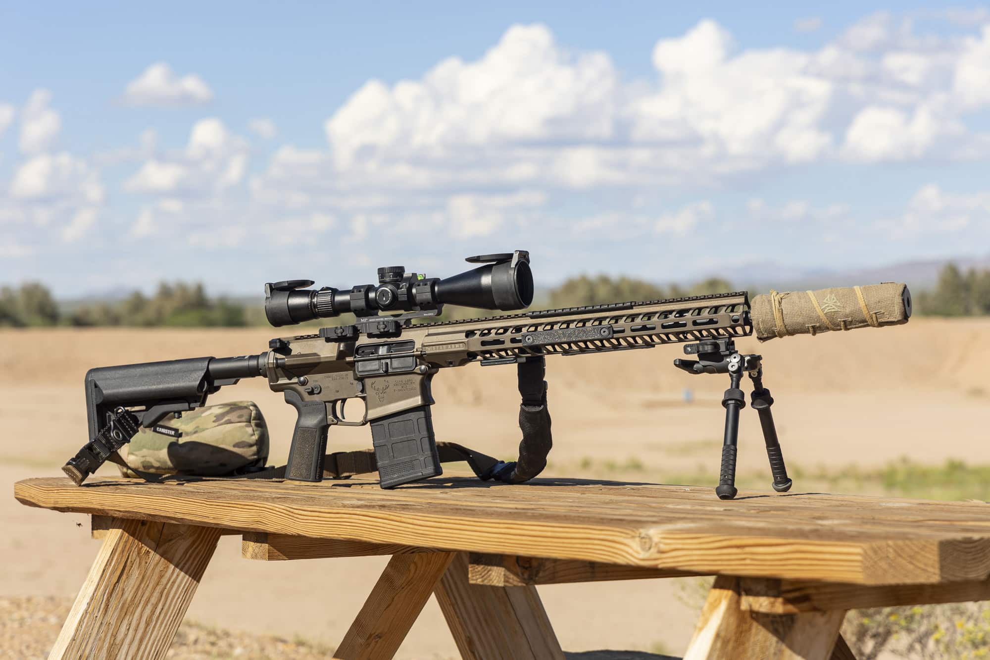 Suppressed AR-10 .308 rifle with scope and bipod on a shooting bench at an outdoor range