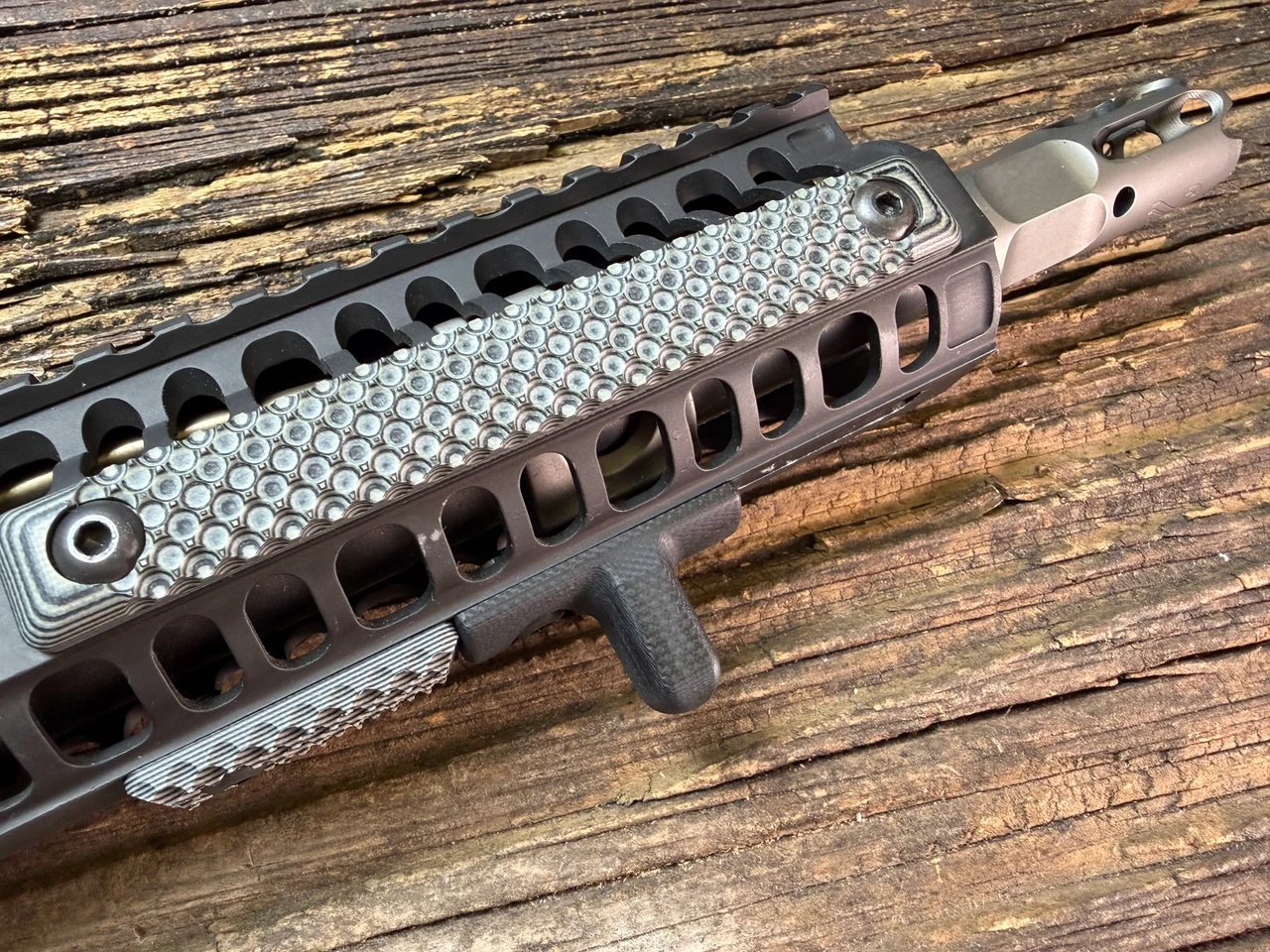 Close-up of a skeletonized KeyMod AR-15 handguard with textured G10 rail covers installed and a small vertical foregrip attached, resting on a wooden surface.