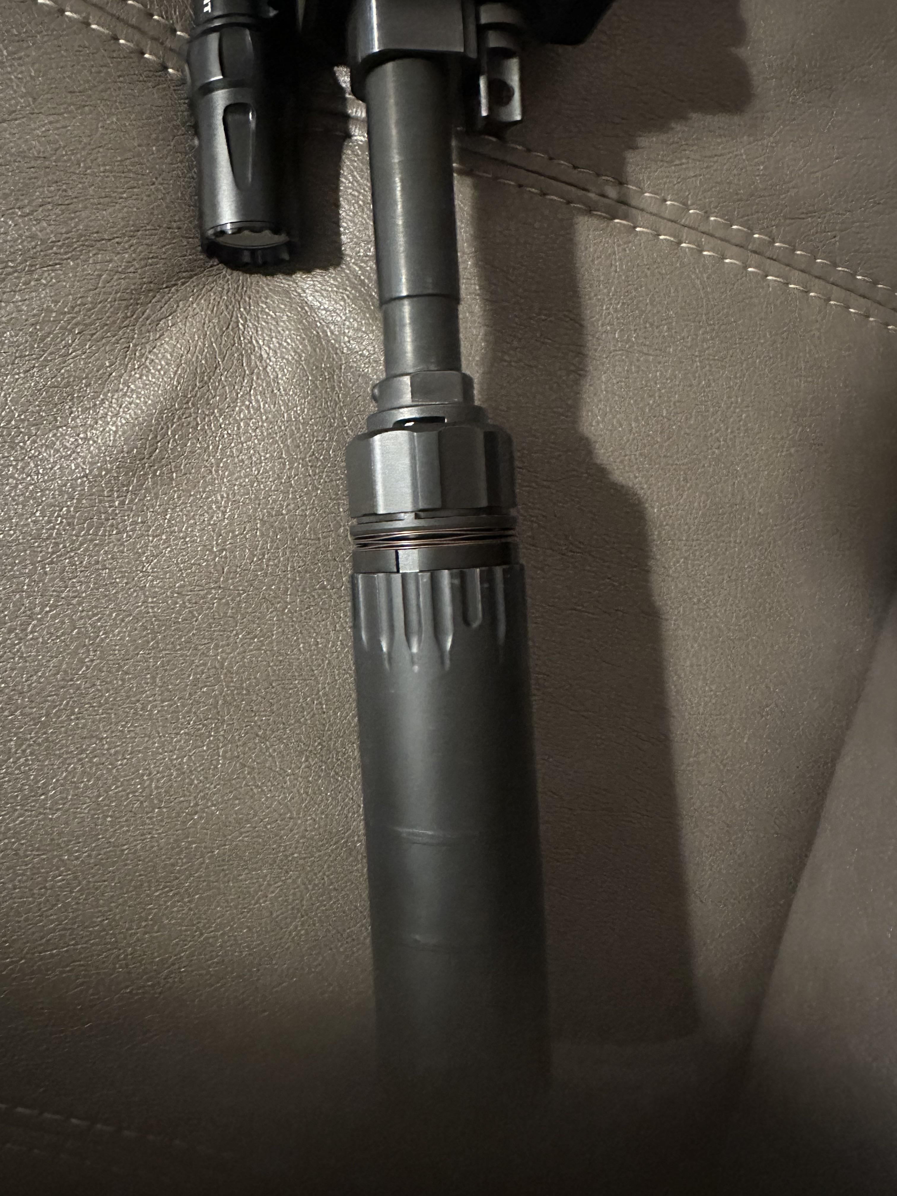 Suppressor attached to AR-15 barrel via quick-detach mount, showing locking collar and cylindrical suppressor body.