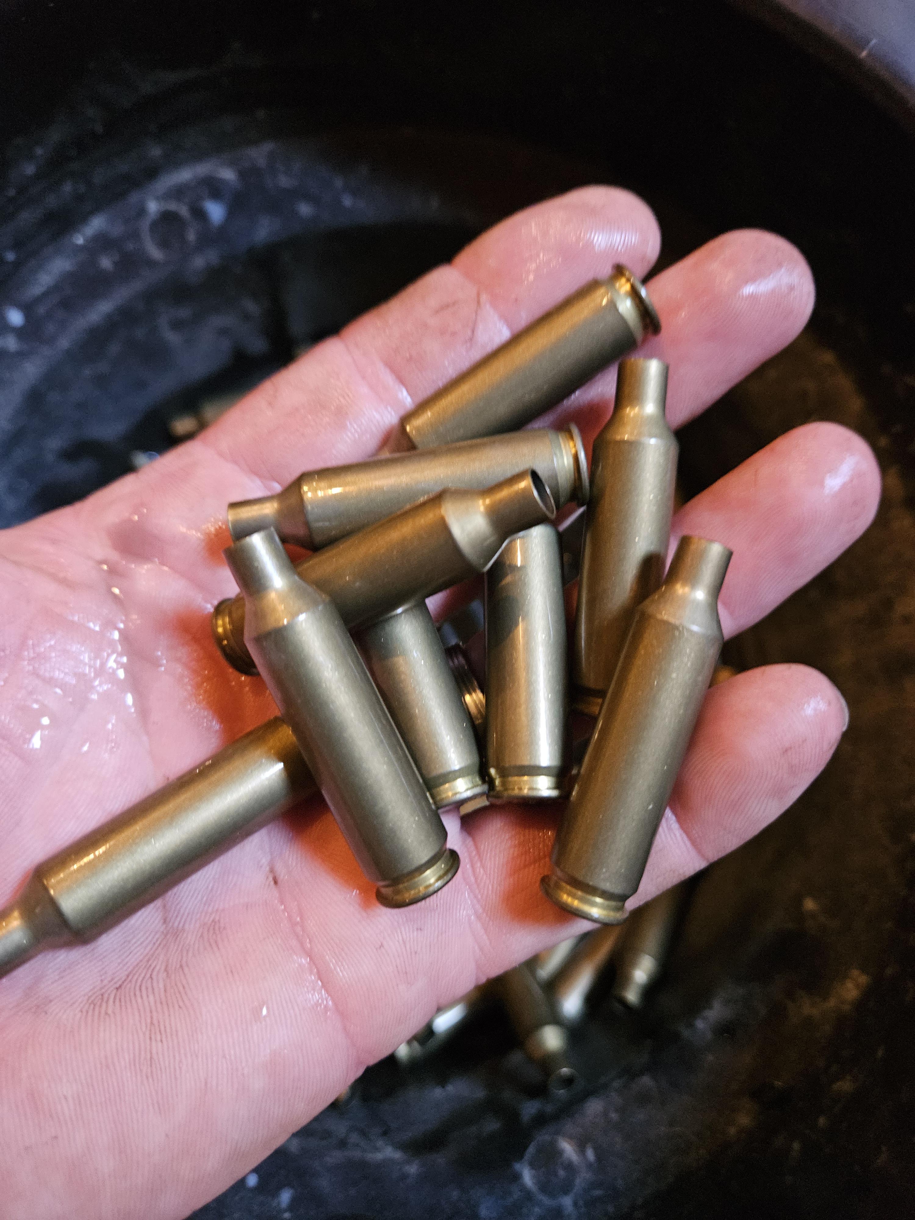 A hand holding several wet, freshly tumbled rifle brass cases over a tumbler bowl