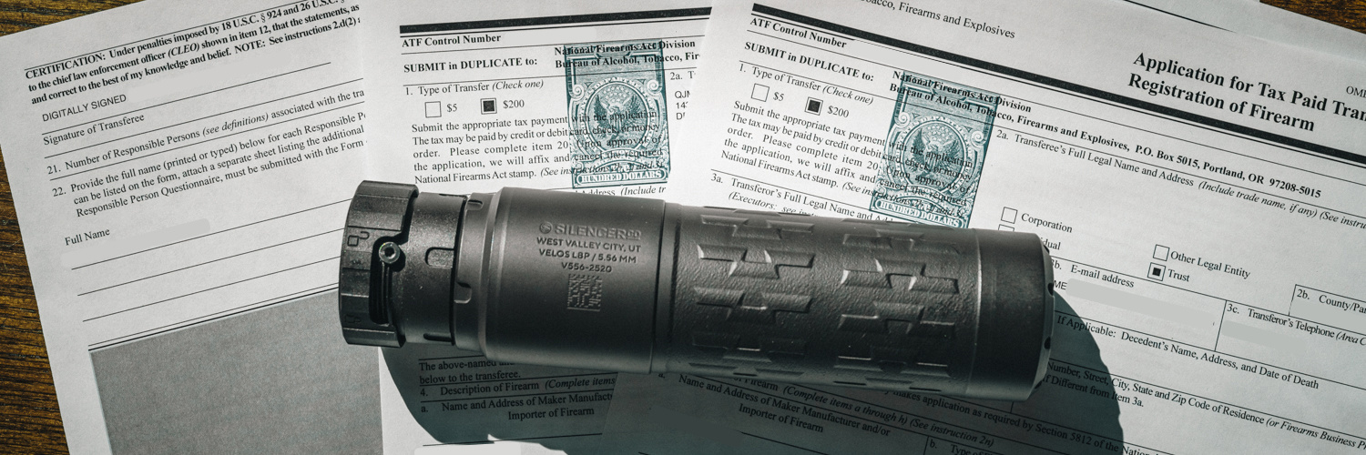 SilencerCo Velos LBP suppressor placed on top of two ATF Form 4 NFA transfer documents on a wooden surface.