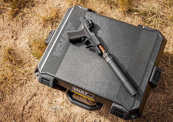Semi-automatic pistol with suppressor attached, laid on top of a closed black Vault hard case outdoors.