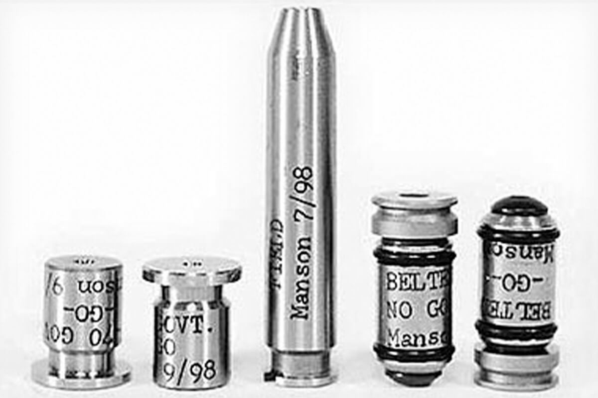 Five Manson headspace gauges and a chamber cast arranged in a row, labeled with go, no-go, and belt no-go designations, photographed in black and white.