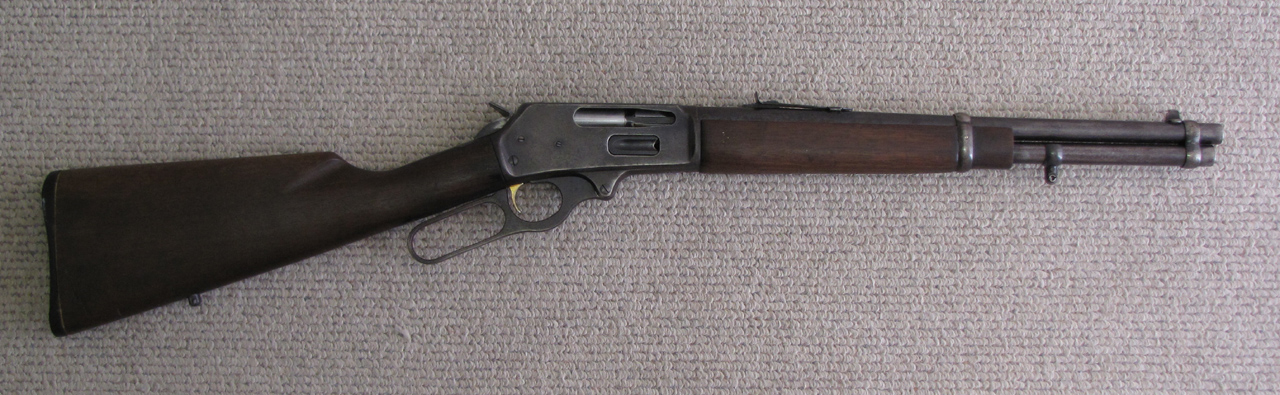 Marlin 336 lever-action rifle with walnut stock and blued finish laid flat on a gray textile surface.