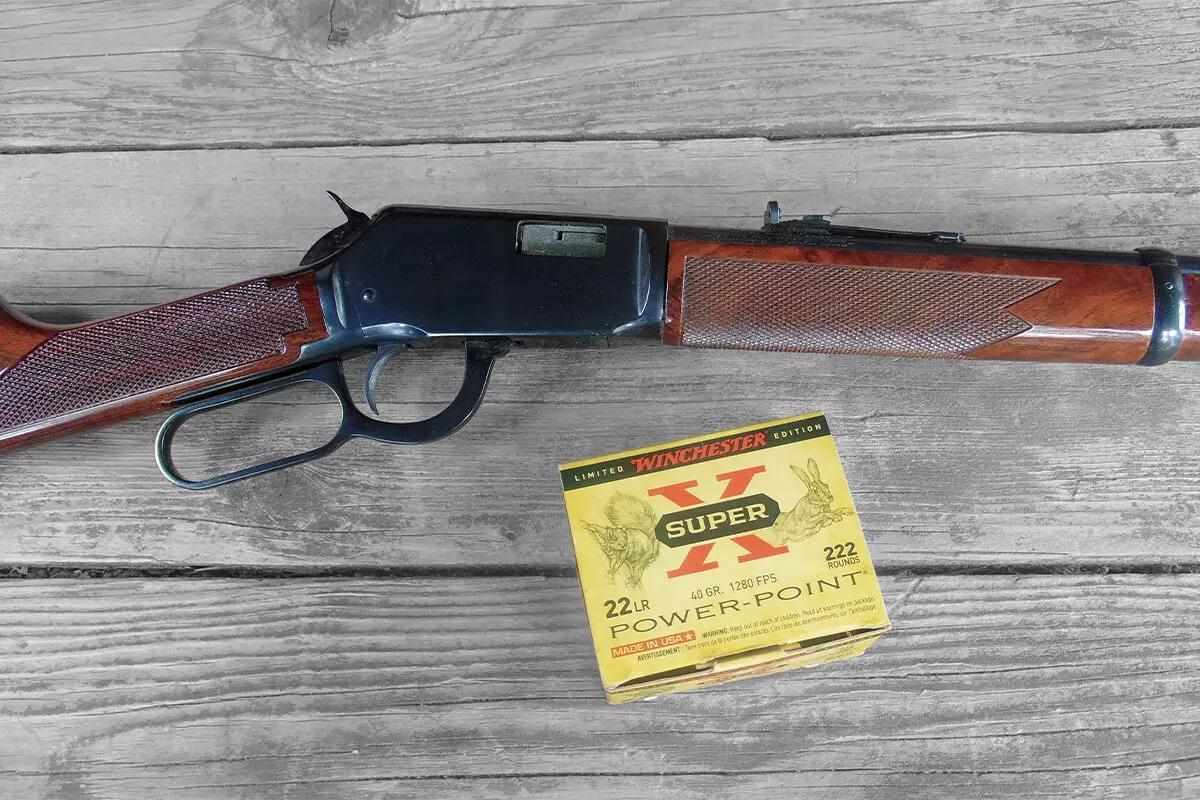 Winchester 9422 lever-action rifle in .22 LR lying on a wooden surface next to a box of Winchester Super-X Power-Point .22 LR ammunition.