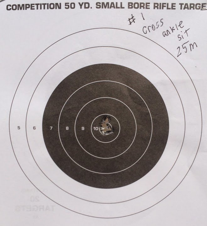 Competition 50-yard small bore rifle target with bullet holes clustered in the 10-ring, annotated with handwritten notes indicating cross-ankle sitting position at 25 meters.