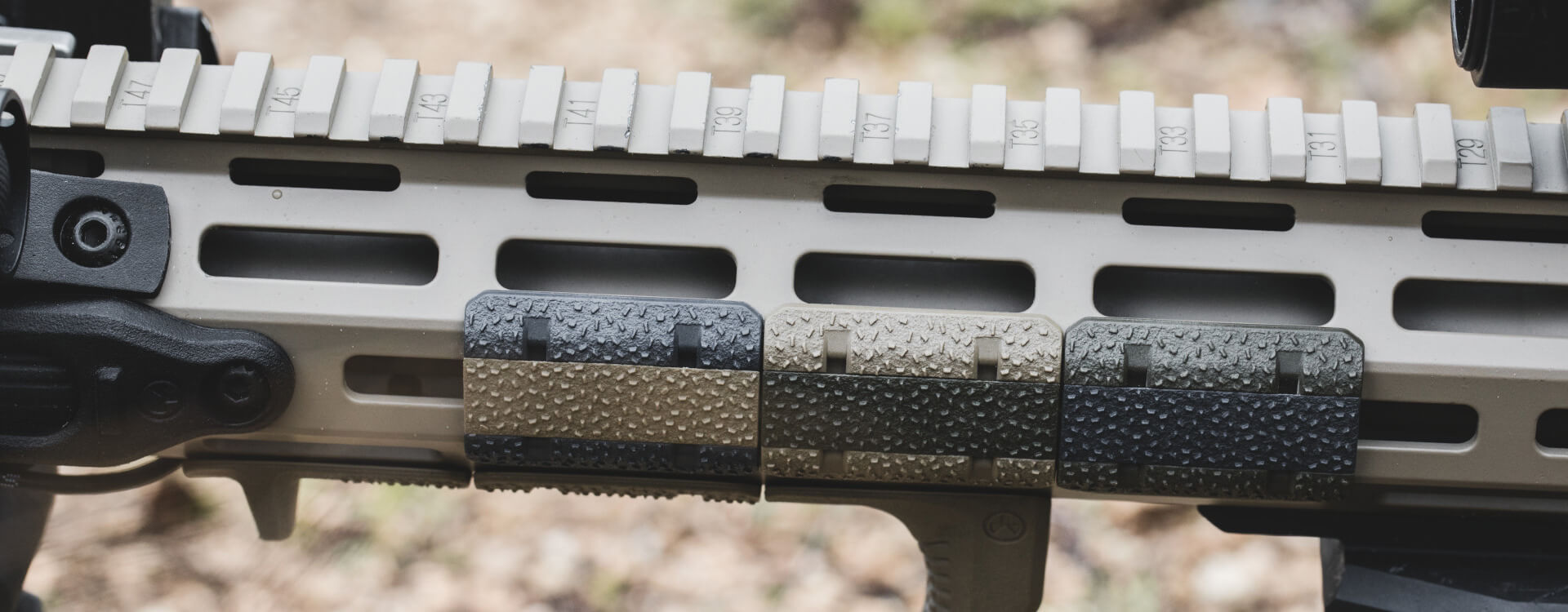 Close-up of three M-LOK rail covers with stippled texture attached to a tan AR-15 handguard with a full-length top Picatinny rail.
