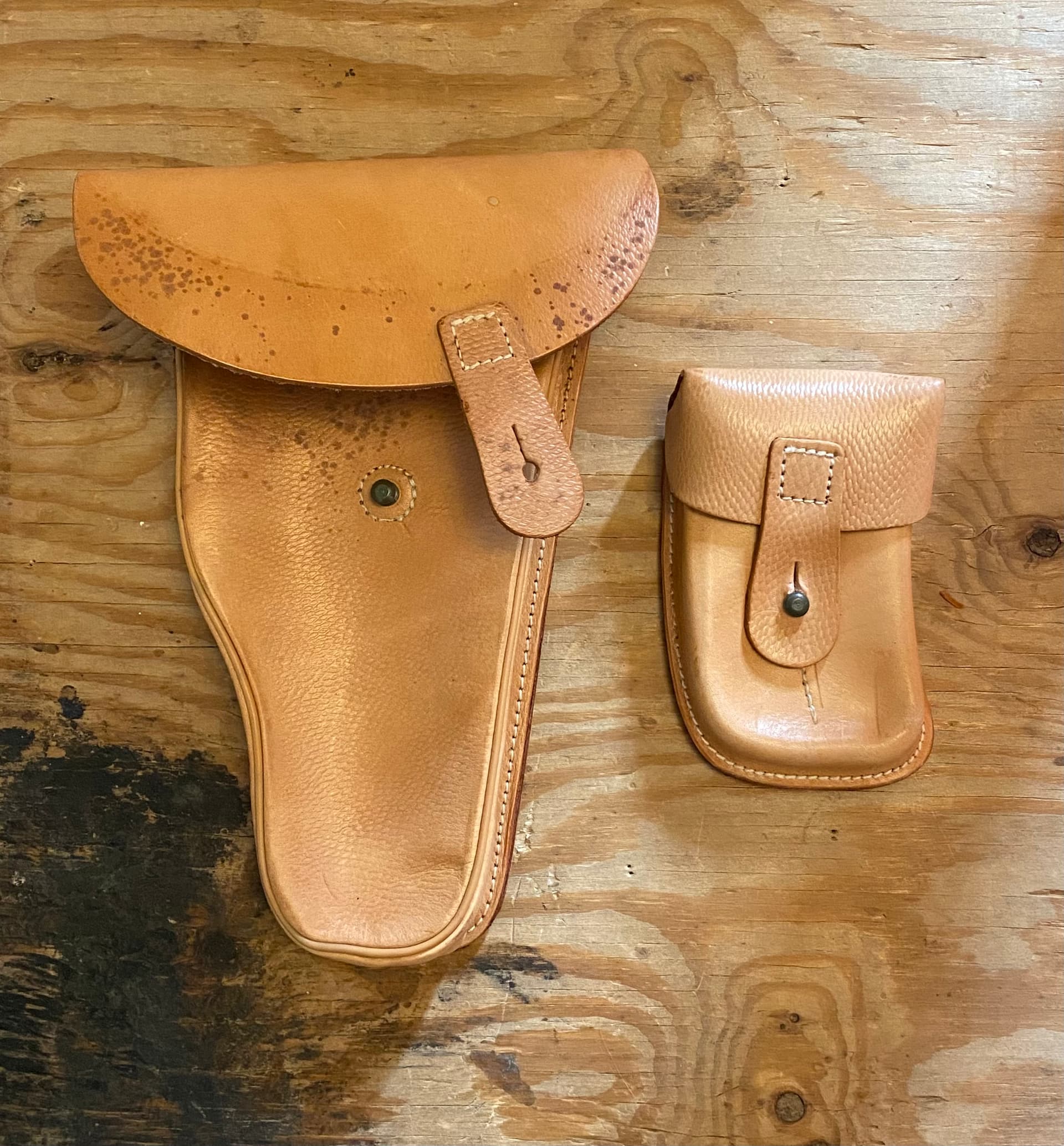 Tan leather surplus military pistol holster and accessory pouch laid flat on a wooden surface.