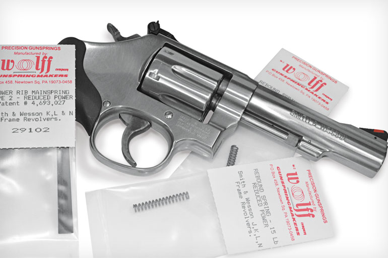 Stainless Smith and Wesson revolver lying next to Wolff Precision Gunsprings replacement mainspring and rebound spring packages on a white background.