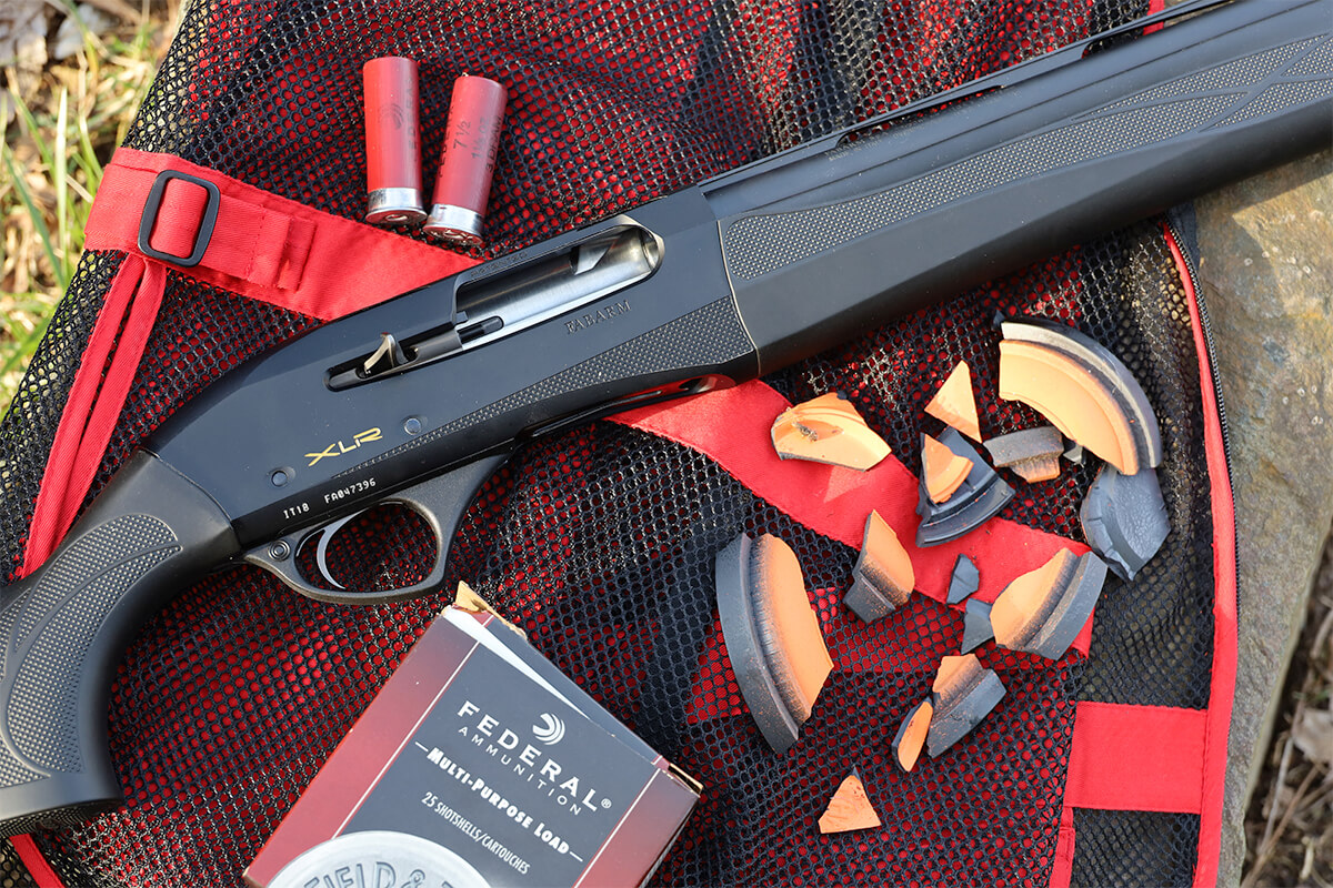 Fabarm XLR semi-automatic shotgun lying on a red mesh shooting bag next to broken clay target pieces and a box of Federal Multi-Purpose shotshells.