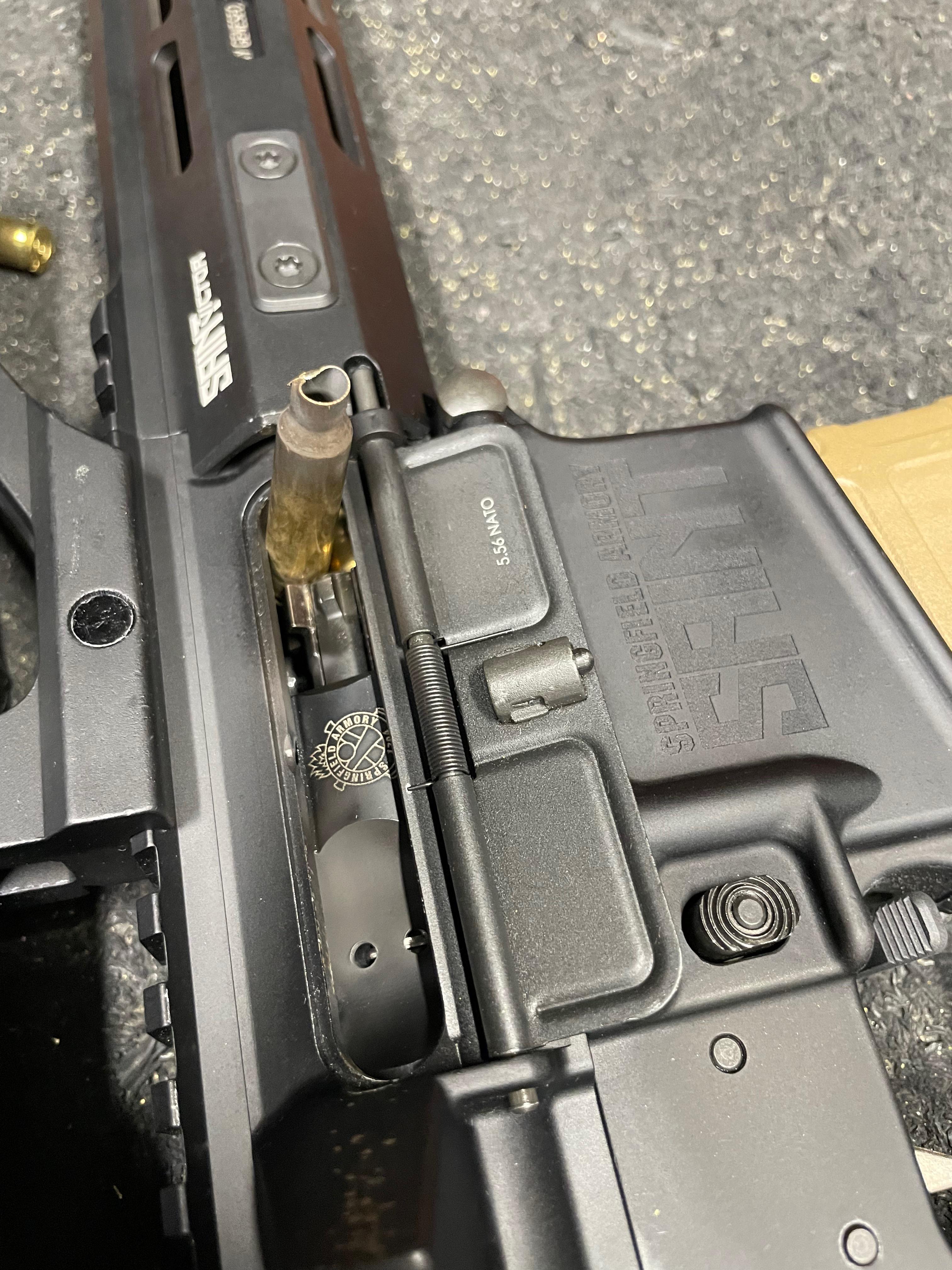 Close-up of a Springfield Armory SAINT 5.56 NATO upper receiver with a stovepiped brass case caught vertically in the open ejection port.