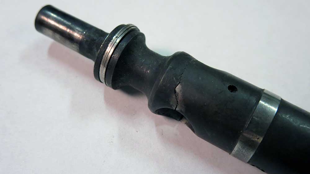 Close-up of a severely cracked rubber buffer component on a cylindrical metal assembly, showing visible fractures and a small hole in the degraded rubber.
