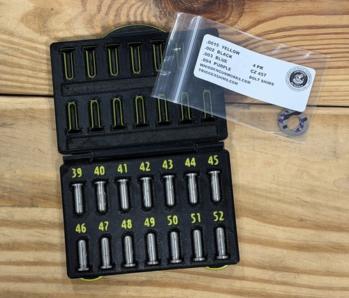 Open black case containing numbered bolt shims for a CZ 457 rimfire action, with a labeled TriggerShims assortment pack on a wood surface.