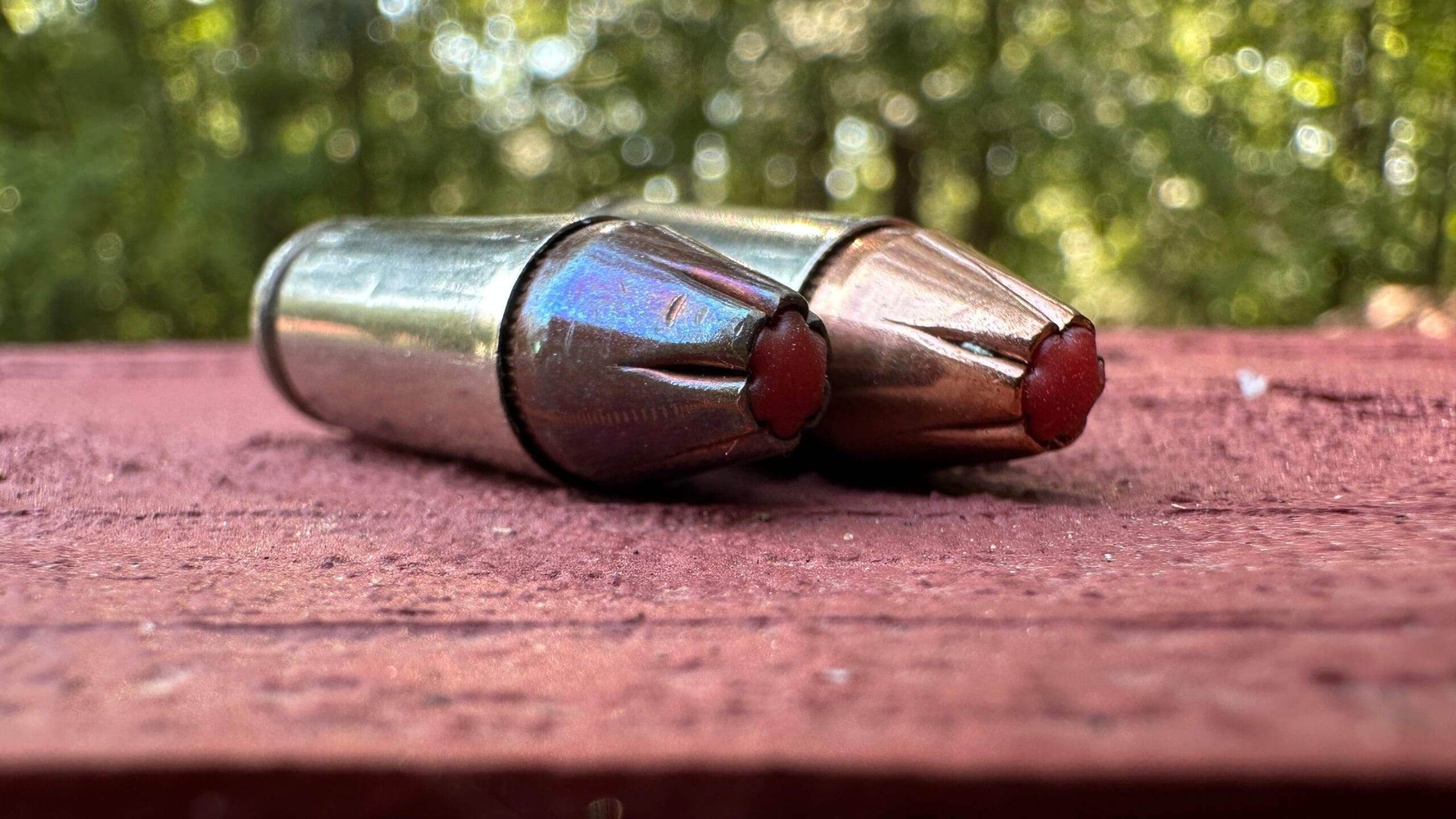 Two polymer-tipped hollow point pistol cartridges resting on a wooden surface outdoors.