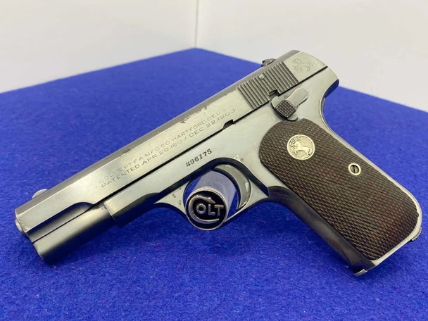 Left side view of a Colt Model 1903 Pocket Hammerless pistol with blued finish and checkered hard rubber grips featuring a Colt rampant colt medallion, displayed on a blue surface.